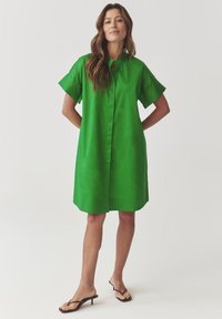 Green short-sleeve dress with a button-down front, collar, and knee-length hem. Smooth fabric with a solid color and relaxed fit.