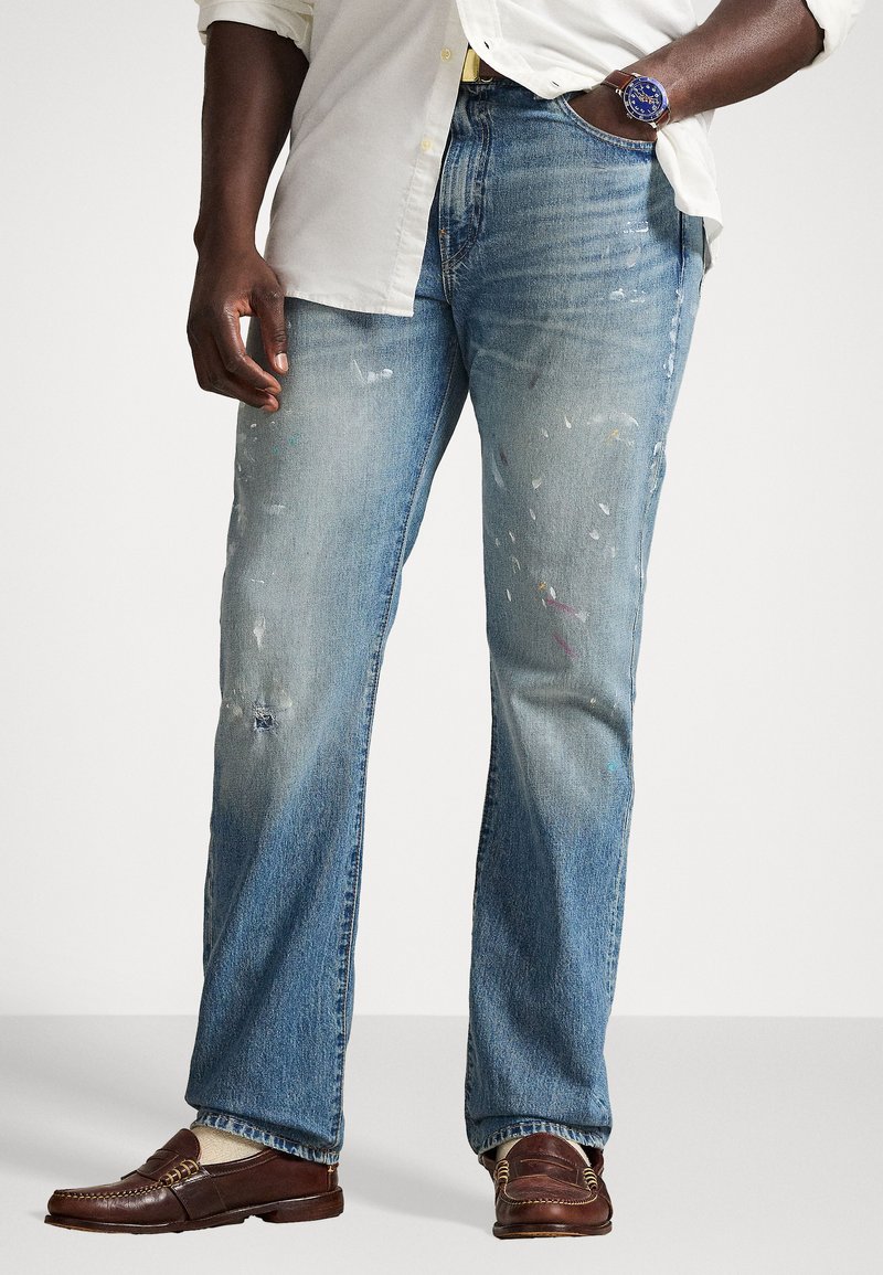 Jasnoniebieskie dżinsy z postrzępionym dołem, przetarciami i plamami farby. Stylizowane z białą koszulą i brązowymi mokasynami.