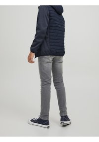 Granatowa kurtka puchowa z kapturem, szare jeansy w slim fit i niebieskie sneakersy. Kurtka ma pikowane detale i gładką teksturę.