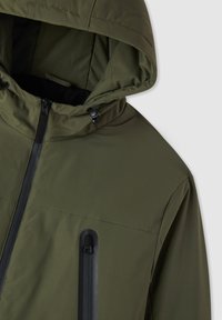 Giacca impermeabile verde oliva con zip frontale, cappuccio regolabile e dettagli neri. Include una tasca nascosta con zip per riporre oggetti.