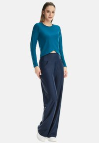 Long-sleeve teal top with a cropped front and curved hem, paired with navy wide-leg pants featuring front pockets and smooth fabric.