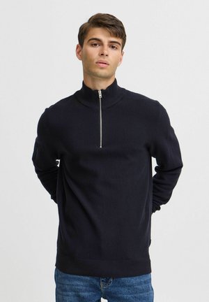 Navy zip-up sweater with a high collar, textured knit pattern, long sleeves, and ribbed hem. Silver zipper detail at the neck.
