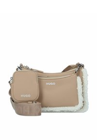 Beige schoudertas met een fluffy witte rand, zilveren hardware en een afneembare tas. Heeft het merklogo in het wit aan de voorkant.