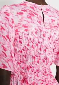 Rosa och vit mönstrad klänning med en texturerad tyg, smocksdetaljer och en nyckelhålsrygg med knappstängning. Korta ärmar.