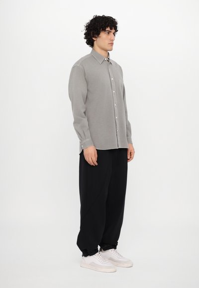 Chemise grise à manches longues avec une poche unique sur la poitrine, associée à un pantalon noir ample et des baskets blanches. Design sobre, sans motifs.