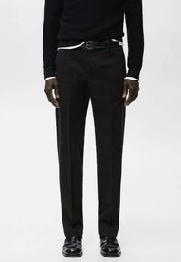 Schwarze, maßgeschneiderte Hose mit geradem Bein aus glattem Stoff. Kombiniert mit einem schwarzen Strickpullover und einem schwarzen Gürtel.