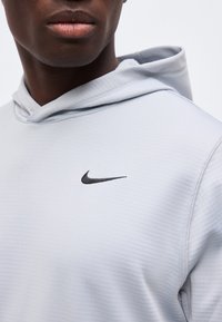 Κοντινό πλάνο ενός ατόμου που φοράει ανοιχτό γκρι φούτερ Nike με μαύρο λογότυπο Nike Swoosh στο στήθος.