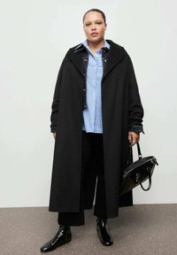 Czarny długi płaszcz na niebieskiej koszuli w paski z ciemną kurtką dżinsową. Czarne spodnie i błyszczące czarne botki. Czarna torebka z uchwytami.