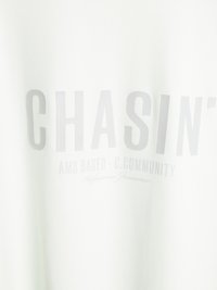 Hanorac alb cu text îngroșat de culoare gri "CHASIN'" pe față, având un text suplimentar, mai mic, dedesubt. Textură netedă a materialului.