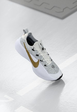 White and gray sneaker with a textured gold Nike swoosh, white laces, and a thick white sole floating above a reflective surface.