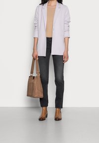 Ljus lavendelfärgad blazer över en beige ribbad topp, parat med mörka jeans och bruna läderskor med anklar. En beige mockaväska hålls i höger hand.