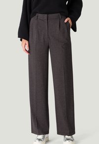 Pantalons larges gris en tissu texturé, avec une taille haute, des plis et des poches latérales. Associés à des baskets métalliques.