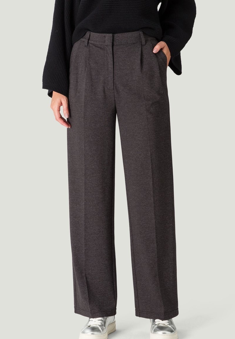 Pantalons larges gris en tissu texturé, avec une taille haute, des plis et des poches latérales. Associés à des baskets métalliques.