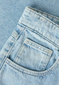Light blue denim fabric with a close-up of a jeans front pocket and stitched seams, showing texture and fabric weave details.