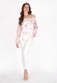Off-the-shoulder hvid bluse med pink blomsterprint, gennemsigtige lange ærmer med flæser, parret med hvide skinny jeans og gyldne høje sandaler.