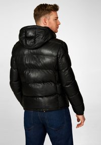 Schwarze Leder-Pufferjacke mit Kapuze, ausgestattet mit einem gesteppte Design, glatter Textur und elastischen Bündchen. Tragen mit blauen Jeans.
