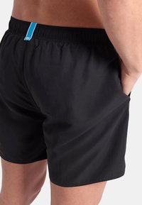 Bañador negro con cintura elástica que presenta una franja azul como detalle. La tela parece suave, ligera y de secado rápido.