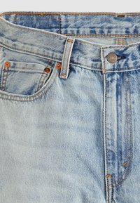 Šviesiai mėlynos džinsinės kelnes su išblukusiu apdorojimu, su vario spalvos mygtuku ir kniedėmis, kontrasto siūlėmis ir standartiniu penkių kišenių dizainu.
