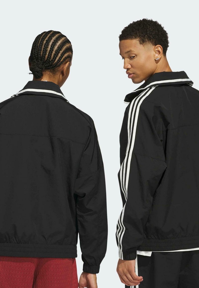 Schwarze Zip-Jacken mit weißen Streifen an den Ärmeln, lockerer Schnitt und elastischen Bündchen. Glattes Material mit sichtbaren Nähdetails.