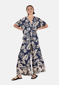 Conjunto de dos piezas en color navy con estampado floral, confeccionado en tejido ligero. Top de manga corta con escote en V, acompañado de pantalones de pierna ancha que presentan un patrón de hojas en color crema.