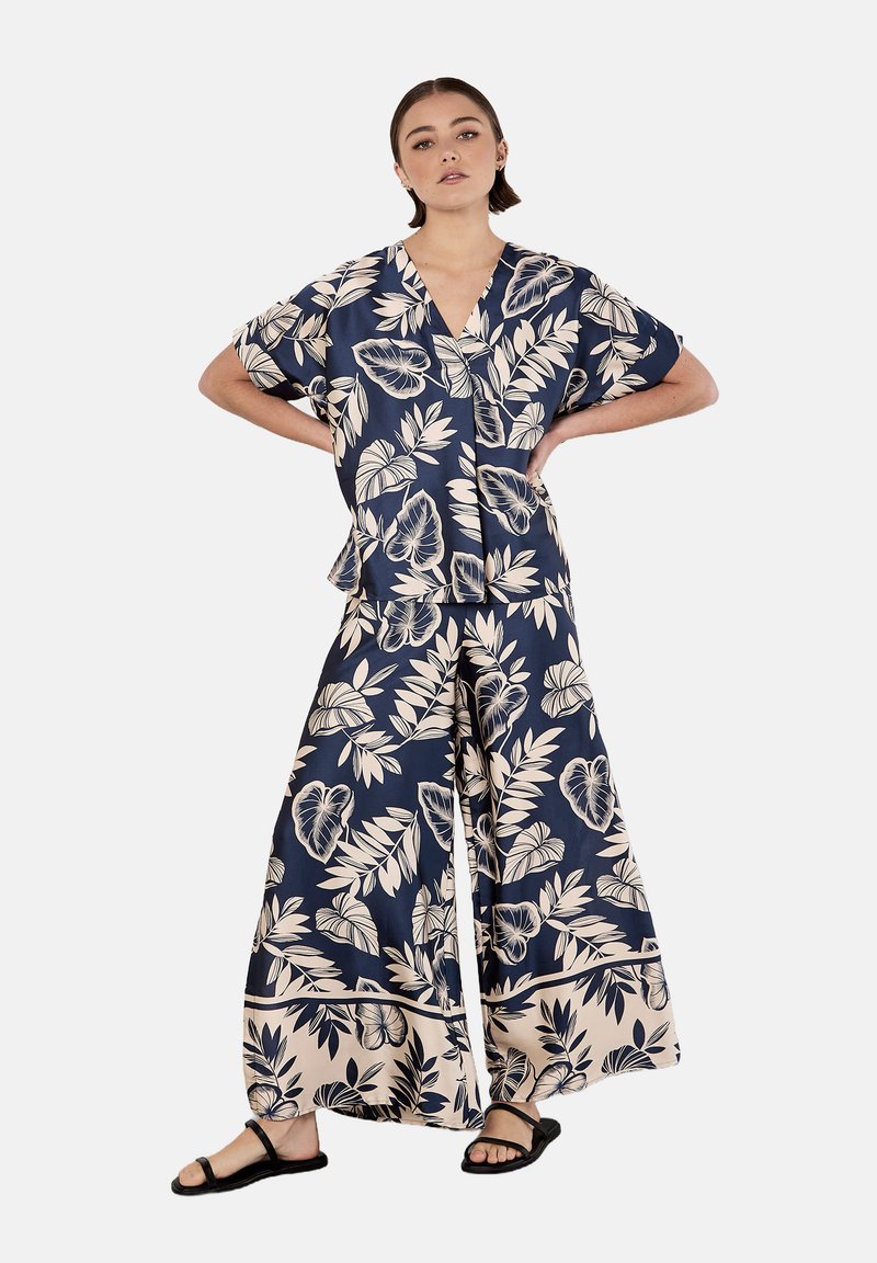 Conjunto de dos piezas en color navy con estampado floral, confeccionado en tejido ligero. Top de manga corta con escote en V, acompañado de pantalones de pierna ancha que presentan un patrón de hojas en color crema.