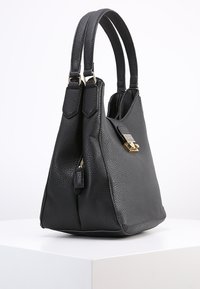 Svart strukturerad läderhandväska med dubbla handtag upptill, dragkedja och detaljer i guldfärg. Har en triangulär form.