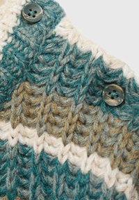 Groboknit tkanina v teal, bež in krem barvah z zigzag vzorcem. Dva ujemajoča gumbka sta pritrjena za zapiranje.