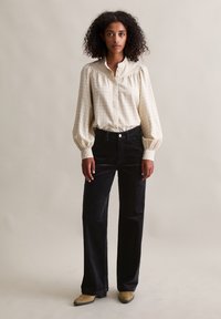 Lichtbeige geruite blouse met pofmouwen, gecombineerd met hooggetailleerde zwarte corduroy broek en beige enkellaarsjes. Eenvoudige knopen sieren de blouse.