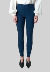 Donkerblauwe broek met hoge taille, gemaakt van rekbare stof. Slim fit die tot de enkel reikt, gecombineerd met zwarte puntige hakken.