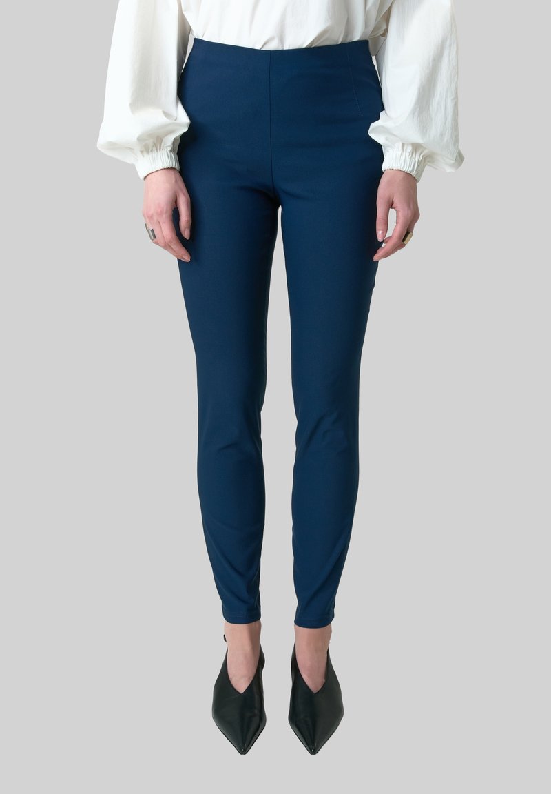 Donkerblauwe broek met hoge taille, gemaakt van rekbare stof. Slim fit die tot de enkel reikt, gecombineerd met zwarte puntige hakken.