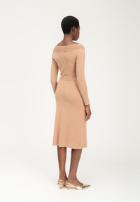 Brede gebreide jurk met schouderloos ontwerp in lichtbeige, getailleerd in de taille, met een midi-length rok. Beschikt over ribbel-details en een zachte textuur.