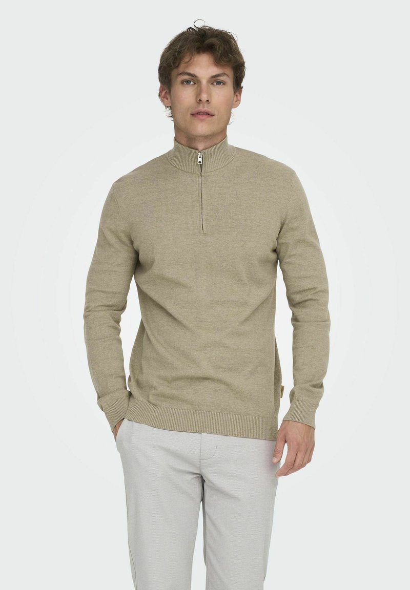 Beiger Pullover mit Reißverschlusskragen und gerippten Bündchen. Hergestellt aus weichem Material, mit feiner Textur und tailliertem Schnitt.