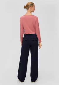 Langärmliges, rosafarbenes Oberteil, kombiniert mit weit geschnittenen, marineblauen Hosen mit Seitentaschen und elastischem Bund.