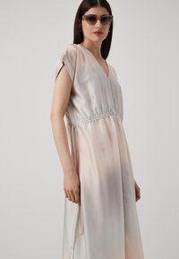 Silkkinen, vaaleanpunainen mekko, jossa on lyhyet hihat, V-pääntie ja kuminauhakettu vyötärö. Mekossa on hienovarainen gradientti ja sivutaskut.