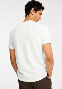Hvid kortærmet t-shirt med et struktureret stof og en rund halsudskæring, der har et diskret firkantet mønster. Bagsidevisning viser en afslappet pasform.