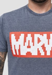 Šedé tričko s kulatým výstřihem, na přední straně má velký pixelový nápis "MARVEL" v červené a bílé barvě. Měkký materiál.