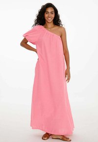 Ružové ľanové maxi šaty s jedným ramienkom, voľný strih a bočné vrecká. Sandále sú obuté pre neformálny vzhľad.