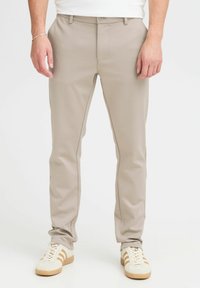Pantalones beige ajustados confeccionados con una tela suave, con un corte slim, trabillas para el cinturón y un cierre de un solo botón. Combinados con zapatillas blancas.