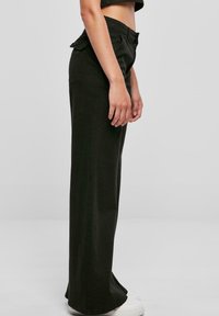 Svarta vida byxor i tyg med hög midja och sidfickor. Plagget har en slät yta och faller rakt ner till fållen.