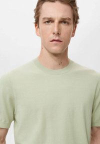 Tricou scurt cu mânecă, verde deschis, cu guler rotund, textură moale, design ajustat, cusături minimale și fără logo-uri sau modele vizibile.