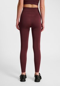 Leggings atletici color bordeaux con fascia alta in vita e design senza cuciture, caratterizzati da una texture liscia e lievi dettagli di contorno sul retro.