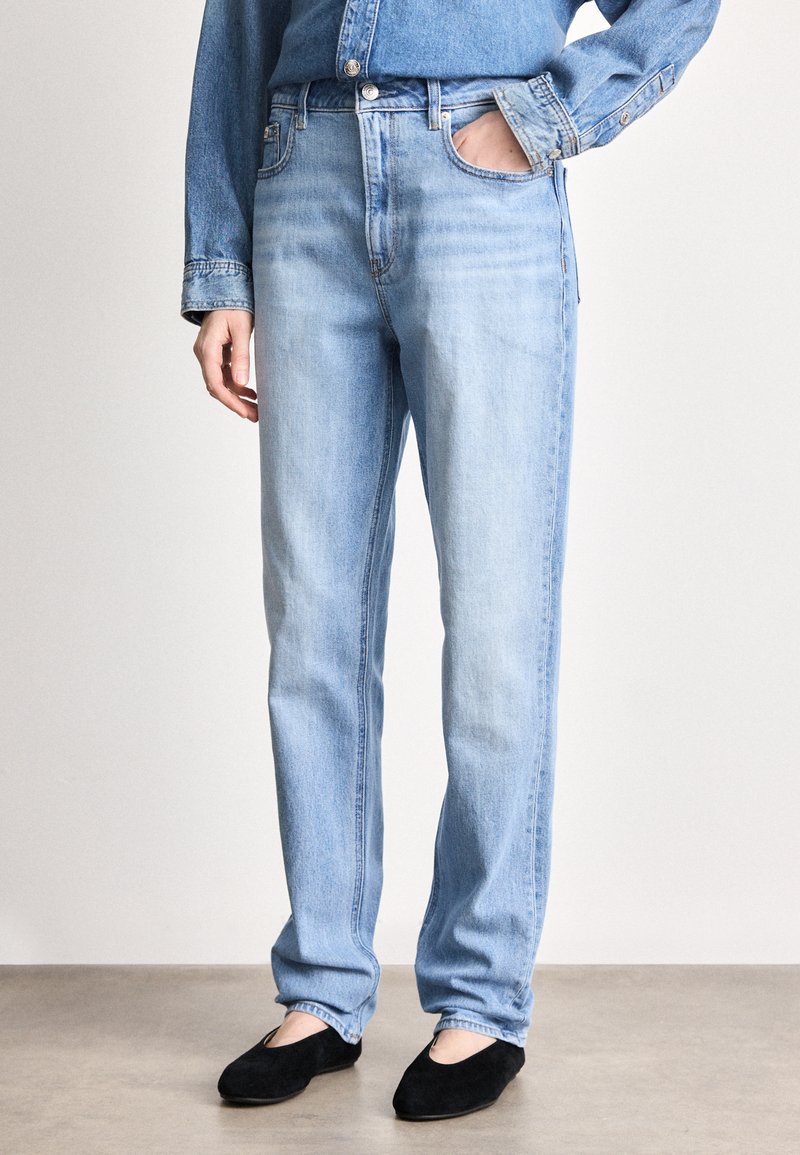 Svijetloplavi traperice s ravnim nogavicama, pet džepova i srednjim strukom, uparene s crnim cipelama.