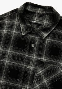 Musta-valkoinen ruudullinen paita, jossa on napitettava kaulus, rintatasku ja tekstuuri, jossa on ruutukuvio. Säännöllinen istuvuus.