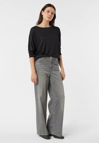 Czarna, luźna bluzka z długim rękawem w połączeniu z szerokimi, jasnoszarymi dżinsami. Dżinsy mają guzik w pasie i boczne kieszenie.