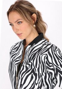 Zebra-print bomberjakke i sort og hvid, med en sort ribbet krave og en guld lynlås. Glat, let stof med en afslappet pasform.
