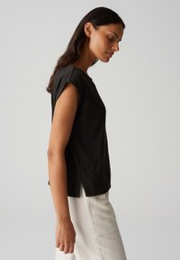 Zwarte gemarmerde kortemouwenshirt met een relaxed fit en zijsplitten, gecombineerd met beige pantalon, die een eenvoudige silhouet toont.