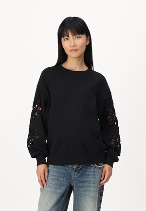 Black sweatshirt with cut-out floral details on sleeves, crew neck, and ribbed hem; worn with light blue distressed jeans.