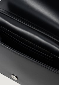 Μαύρη δερμάτινη τσάντα χεριού με λεία υφή, διαθέτοντας ένα μόνο μεταλλικό κούμπωμα και εσωτερικές θήκες για κάρτες. Απλός και λειτουργικός σχεδιασμός.