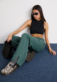 Svart ribbet crop top, grønne vide joggebukser, zebra-mønstrede sko og en svart fake fur-veske. Sitter på blått teppe.