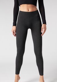 Schwarze Leggings aus einem strukturierten, elastischen Material, mit einem hohen Bund und einer schmalen Silhouette, die an den Knöcheln verjüngt.